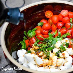 Tomatoes, fresh mozzarella, and basil in a bowl with balsamic vinegar drizzled over the top.