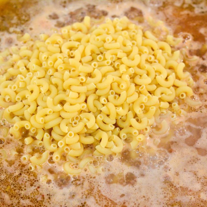 Skillet with ground beef, water, ketchup, mustard, and macaroni for homemade hamburger helper.