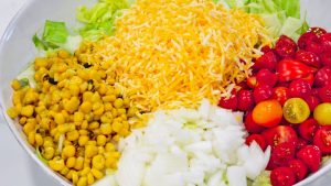 shredded cheese, corn, onions, and tomatoes on top of chopped lettuce for taco salad