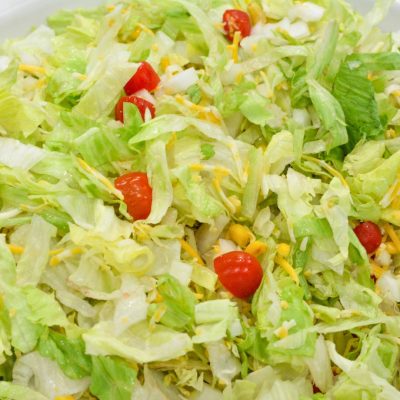 In a large bowl, layer the chopped lettuce, cheese, beans, tomatoes, onion, and corn, or any other desired toppings. Toss the salad.