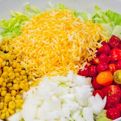 shredded cheese, corn, onions, and tomatoes on top of chopped lettuce for taco salad