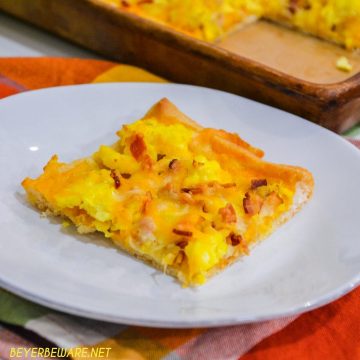 Cheesy bacon breakfast pizza is made with a refrigerated pizza crust, cheese sauce, scrambled egg, and bacon, topped off with more cheese and garlic butter for a decadent breakfast treat.