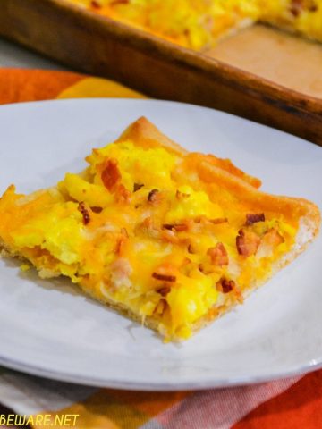 Cheesy bacon breakfast pizza is made with a refrigerated pizza crust, cheese sauce, scrambled egg, and bacon, topped off with more cheese and garlic butter for a decadent breakfast treat.