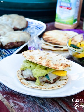 Guacamole burgers combine taco night with burger night straight from the grill with flavorful burgers, pepper-jack cheese, guacamole, sauteed onions, peppers, and street taco tortilla shells.