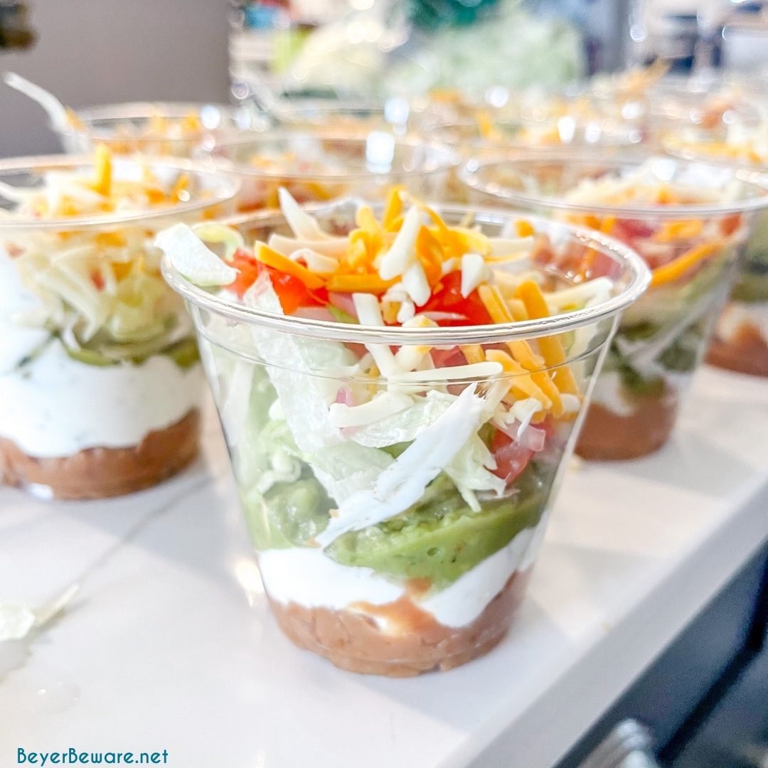 Spicy ranch 7-layer taco dip is Layers of taco-seasoned refried beans, guacamole, sour cream with ranch, lettuce, cheese, pico de gallo, olive, and cheese!