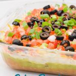 Spicy ranch 7-layer taco dip is Layers of taco-seasoned refried beans, guacamole, sour cream with ranch, lettuce, cheese, pico de gallo, olive, and cheese!