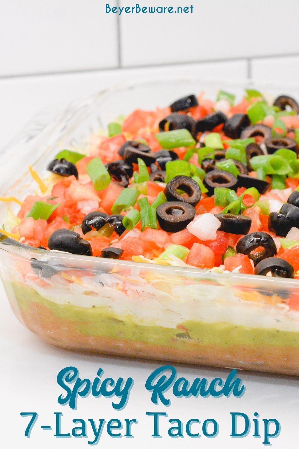 Spicy ranch 7-layer taco dip is Layers of taco-seasoned refried beans, guacamole, sour cream with ranch, lettuce, cheese, pico de gallo, olive, and cheese!