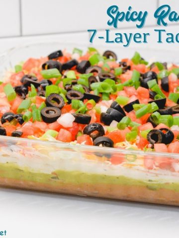 Spicy ranch 7-layer taco dip is Layers of taco-seasoned refried beans, guacamole, sour cream with ranch, lettuce, cheese, pico de gallo, olive, and cheese.