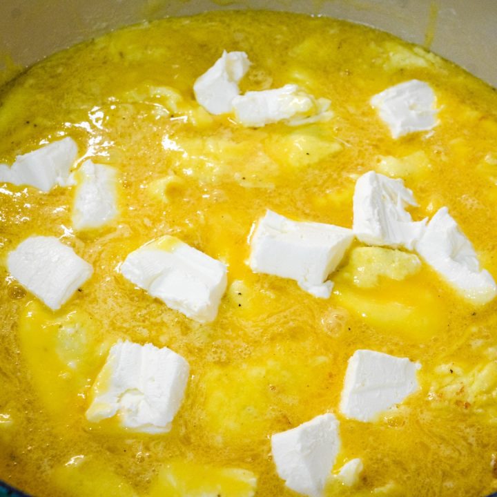 Place the pieces or spoonfuls of cream cheese into the half-cooked eggs. stir to combine and remove from the heat. Pour into the greased crock pot insert.