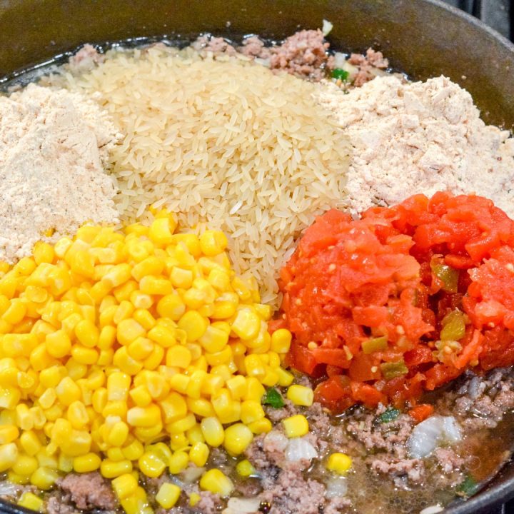 To the browned ground beef, add the rice, flavor packets, canned tomatoes and chilis, and corn. Slowly add the water.