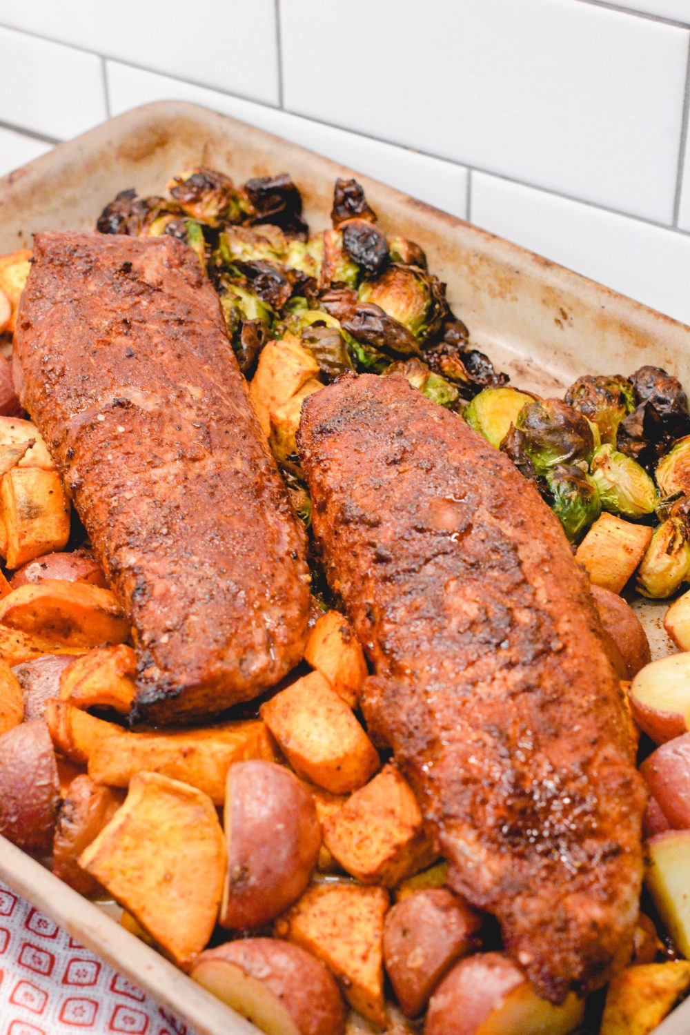 The sheet pan pork tenderloin is rubbed in a sweet and spicy dry rub that is sprinkled on the cut-up sweet potatoes, red potatoes, and Brussels sprouts before it is oven baked. 