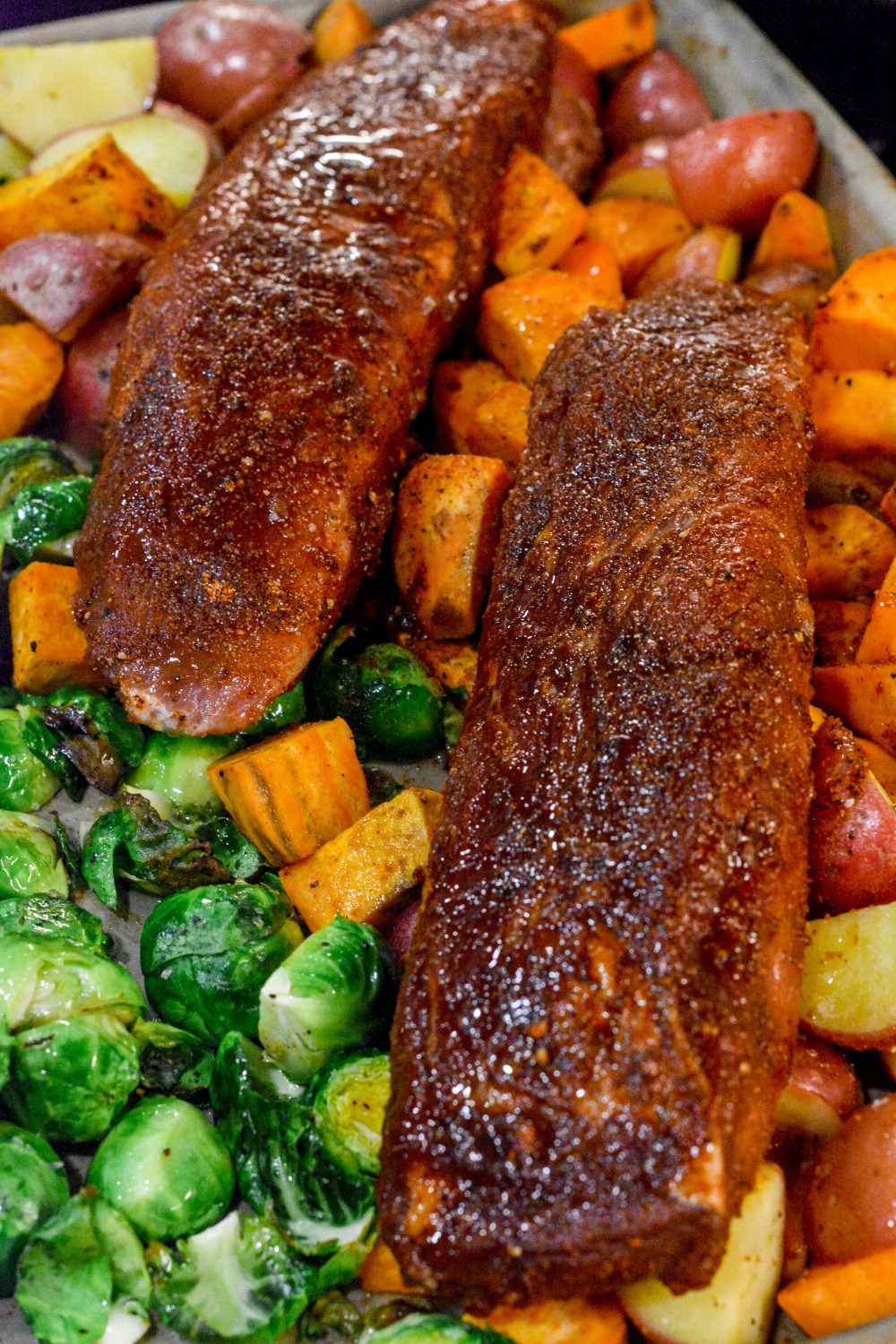 The sheet pan pork tenderloin is rubbed in a sweet and spicy dry rub that is sprinkled on the cut-up sweet potatoes, red potatoes, and Brussels sprouts before it is oven baked.