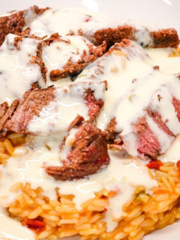 Then place the sliced steak on top of the rice. Finally drizzle the queso over the top of the steak. And the results are arroz con carne just like you would get at your local Mexican Restaurant.