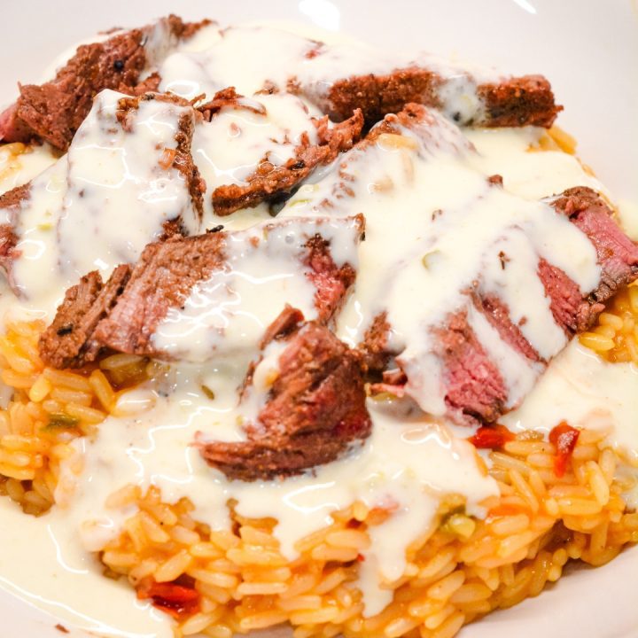 Then place the sliced steak on top of the rice. Finally drizzle the queso over the top of the steak. And the results are arroz con carne just like you would get at your local Mexican Restaurant.