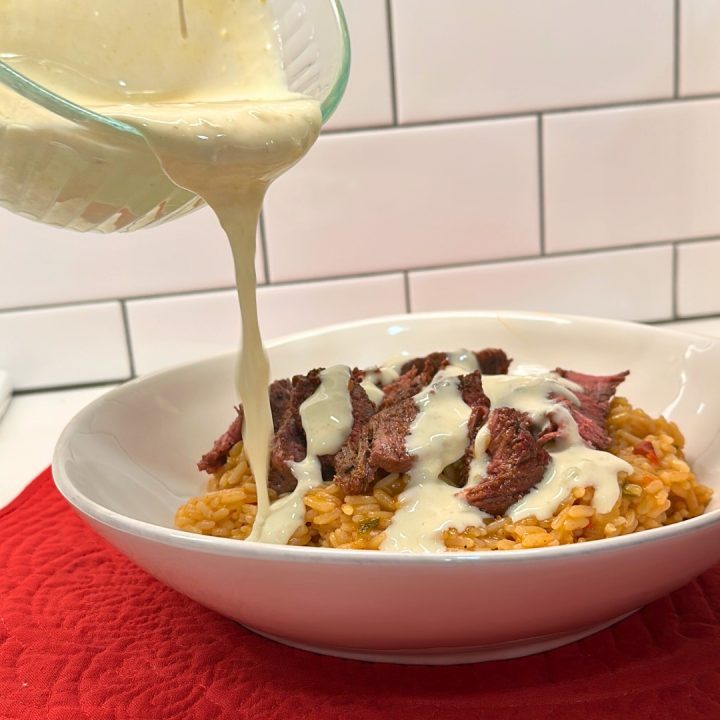 Then place the sliced steak on top of the rice. Finally drizzle the queso over the top of the steak. And the results are arroz con carne just like you would get at your local Mexican Restaurant. 