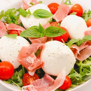 Sprinkle the burrata arugula salad with salt and pepper and add in basil leaves.