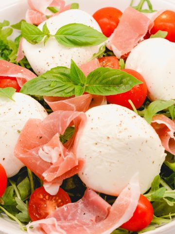 Sprinkle the burrata arugula salad with salt and pepper and add in basil leaves.