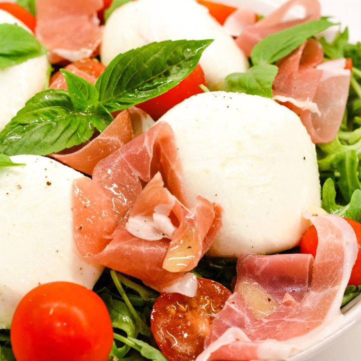 Arugula salad with its perfect balance of peppery greens, salty prosciutto, fresh tomatoes, velvety burrata, and refreshing basil topped with a homemade vinaigrette.
