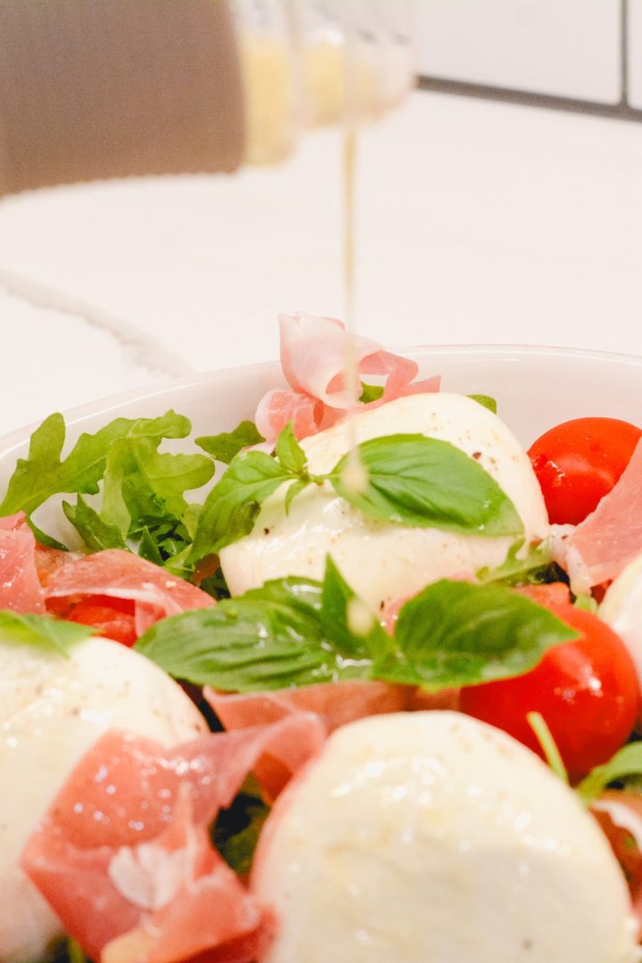 Arugula salad with its perfect balance of peppery greens, salty prosciutto, fresh tomatoes, velvety burrata, and refreshing basil topped with a homemade vinaigrette. 