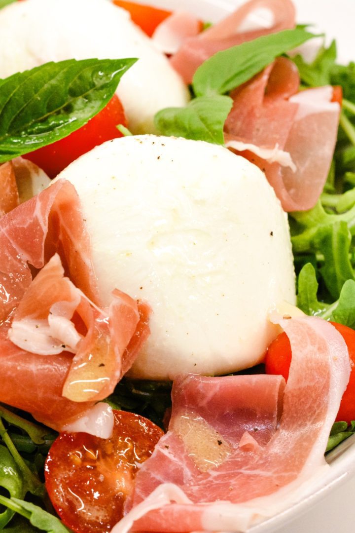 Arugula salad with its perfect balance of peppery greens, salty prosciutto, fresh tomatoes, velvety burrata, and refreshing basil topped with a homemade vinaigrette.