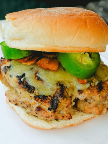 These jalapeno popper stuffed pork burgers are made with ground pork and filled with cream cheese, fresh jalapeno slices, and bacon pieces then topped with even more cheese for the perfect spicy pork burgers recipe.