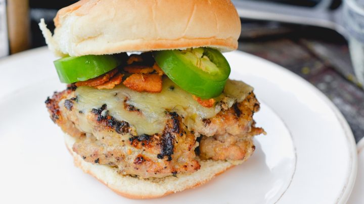 These jalapeno popper stuffed pork burgers are made with ground pork and filled with cream cheese, fresh jalapeno slices, and bacon pieces then topped with even more cheese for the perfect spicy pork burgers recipe.