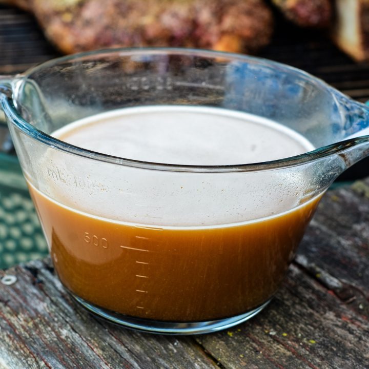 A measuring cup filled with beef broth to baste onto smoked beef roast.