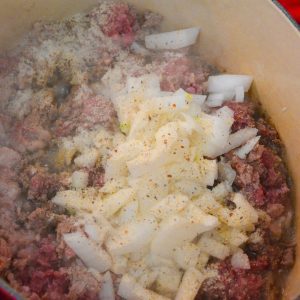 Begin by browning the ground beef. Cook the ground beef until it is almost completely browned, then stir in the onions and garlic.