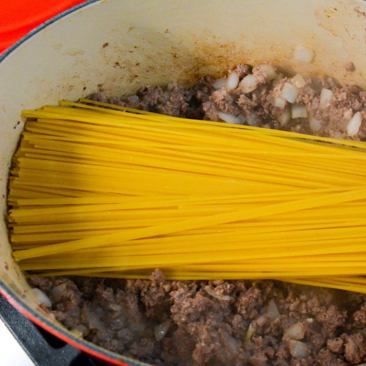 When the onions are just beginning to become translucent, drain any fat off the meat and then add the tomato sauce. Top with the dry spaghetti noodles.