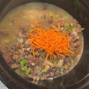 Into the crock pot dump the potatoes, carrots, and hamburger mixture. Pour the chicken and beef broth over the mixture and top off with the cream cheese.