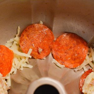 Prep a bundt pan by spraying it with cooking spray. In the bottom of the pan place pepperonis around the bottom.