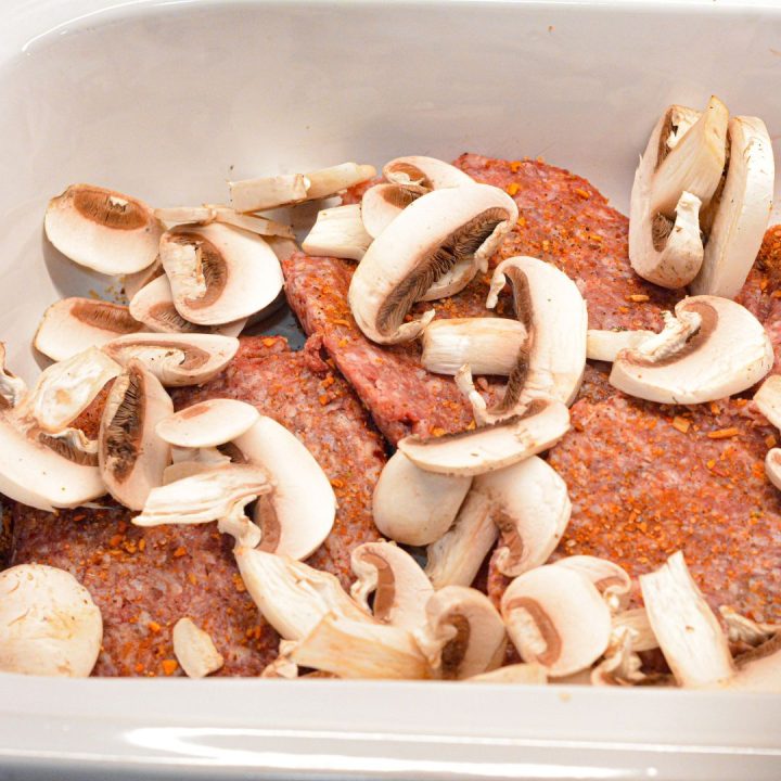 Start by placing the frozen hamburger patties in the crock pot. Season each patty with steak seasoning. After one layer of hamburgers spread half the sliced mushrooms over the top. 