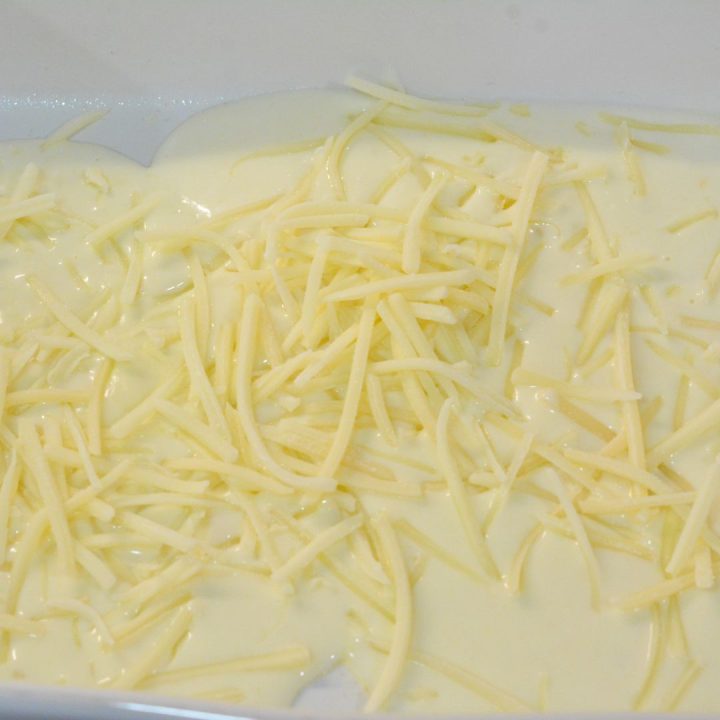 Start layering the scalloped potatoes by pouring ¼ of the white sauce in the bottom, then a layer of Gruyere cheese.