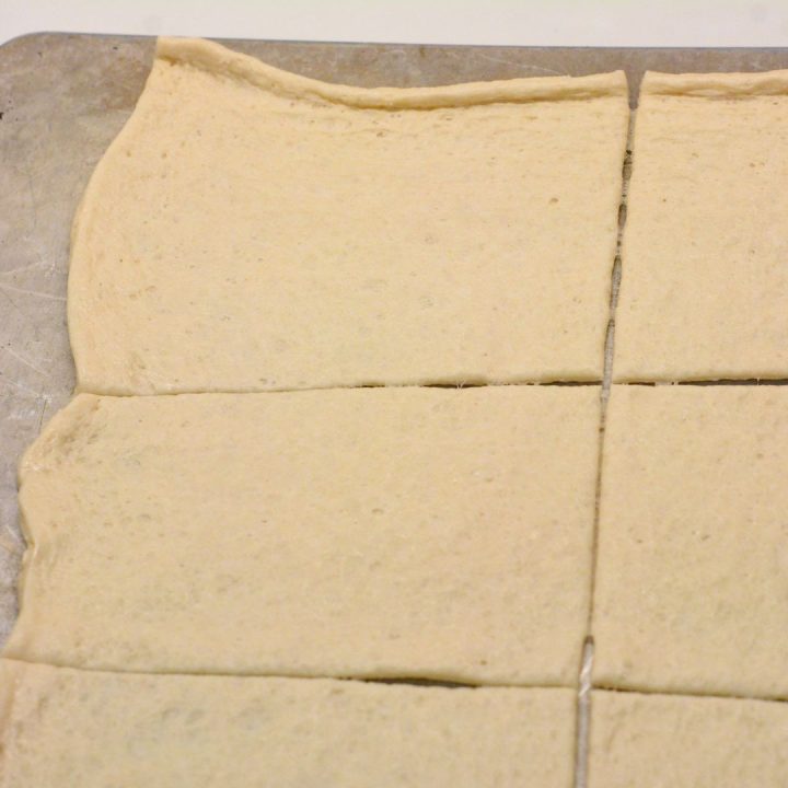 Pop open the can of pizza dough and stretch the dough out on a baking sheet. Then cut into eight rectangle pieces.