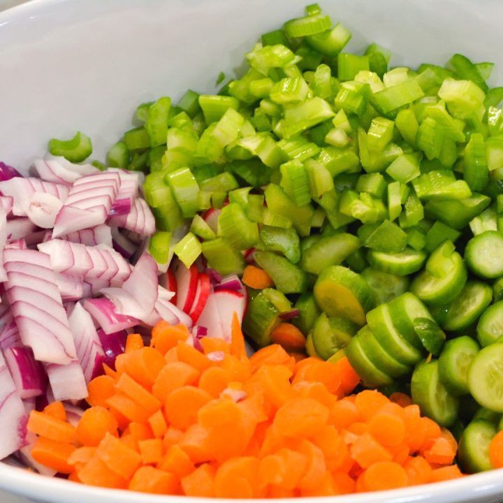 While the spaghetti is cooling, prepare the vegetables. Halve the cherry tomatoes, dice the cucumbers, celery, carrots and bell pepper, slice the radishes, and finely chop the red onion.