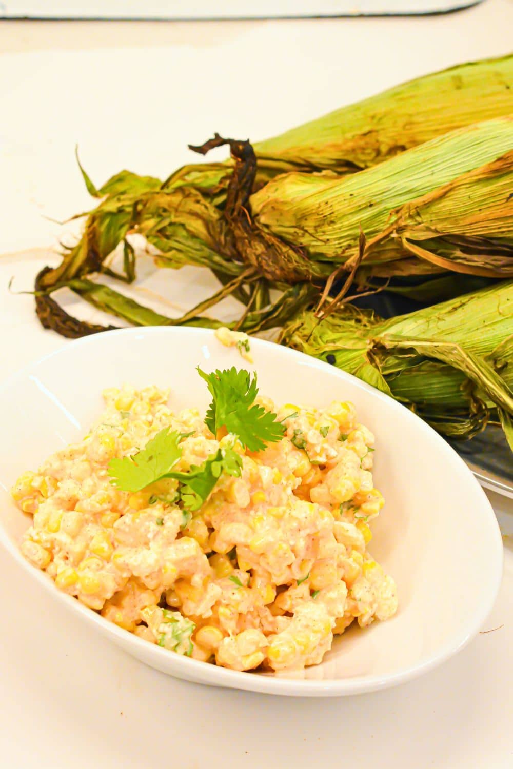 Creamy Mexican street corn salad in a white bowl topped with queso fresco cheese and cilantro