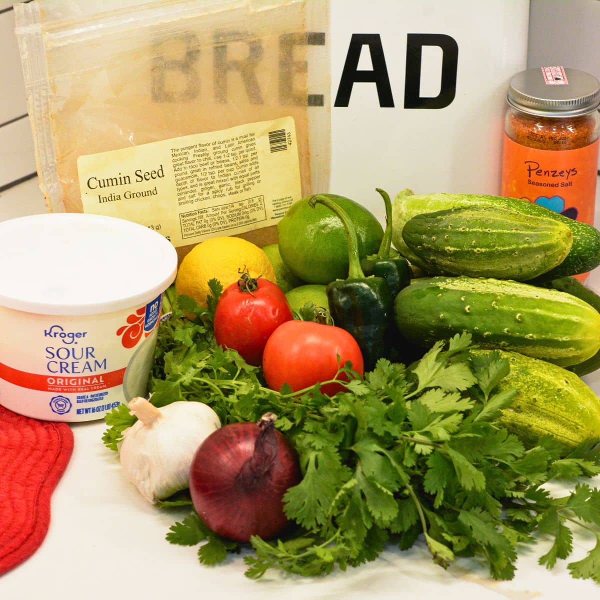Cucumbers, tomatoes, jalapeños, red onion, garlic, and sour cream ingredients for cucumber salsa on a kitchen counter