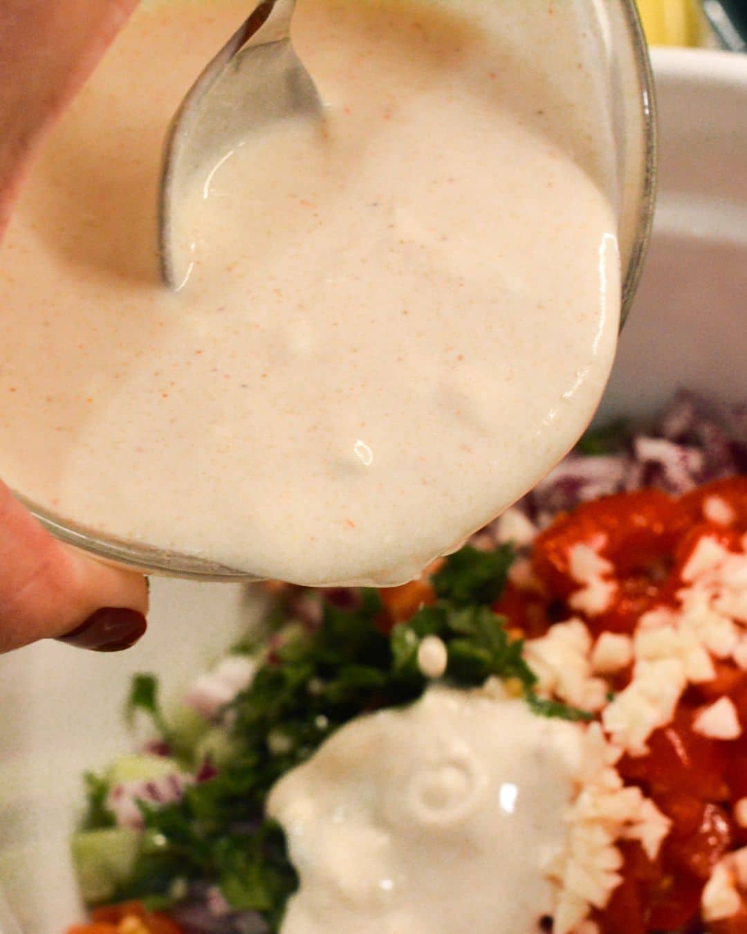 Sour cream dressing pouring into bowl of cucumber, tomato, and onion